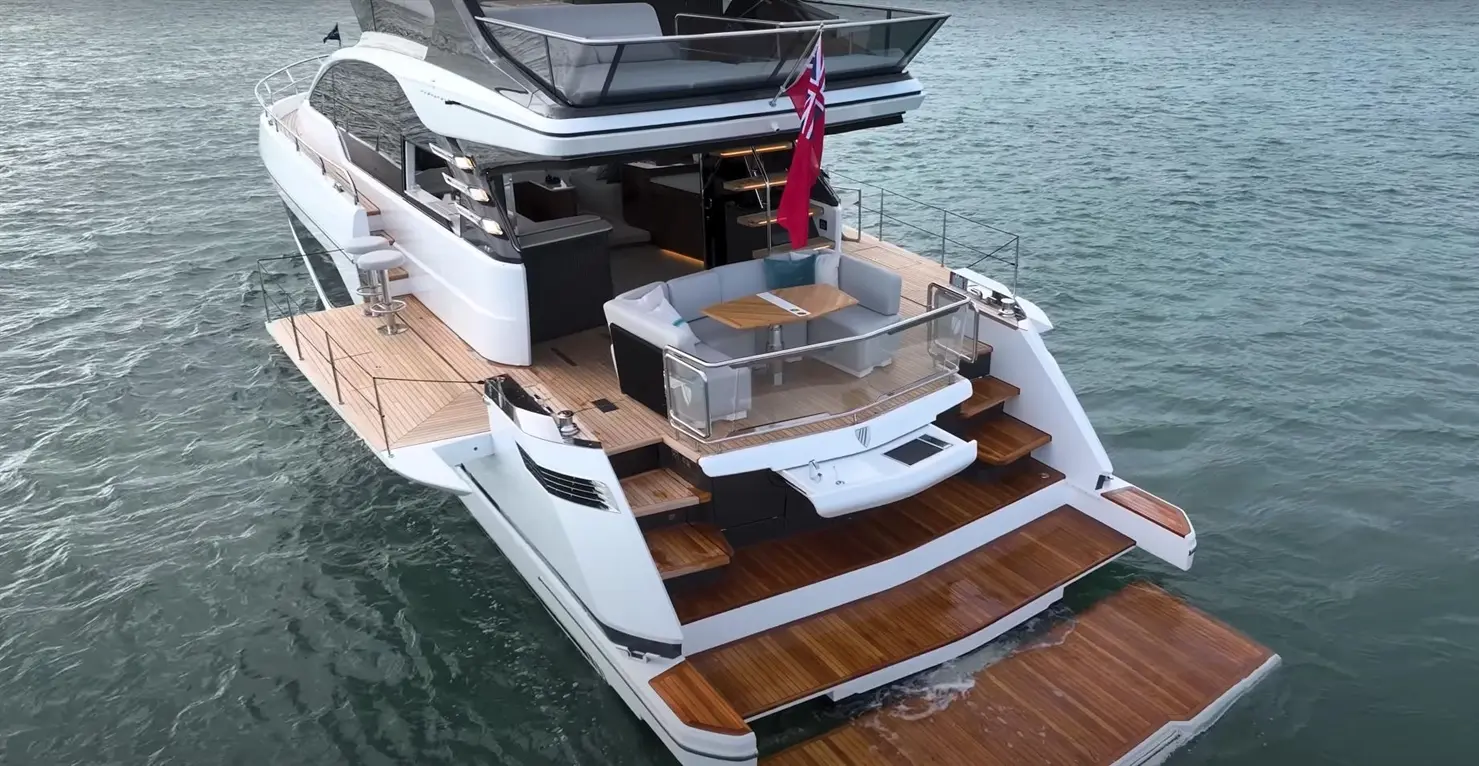 Luxury yacht featuring a spacious deck, modern seating area, and a distinctive red flag, anchored in calm waters.